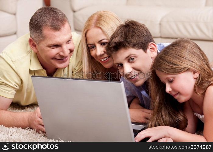 Happy family of four browsing on laptop as they relax on carpet in living room