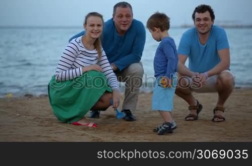 Happy family of four looking to the camera at the seaside in the evening