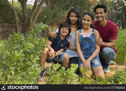 Happy family of man woman son and daughter sitting in a garden and posing.