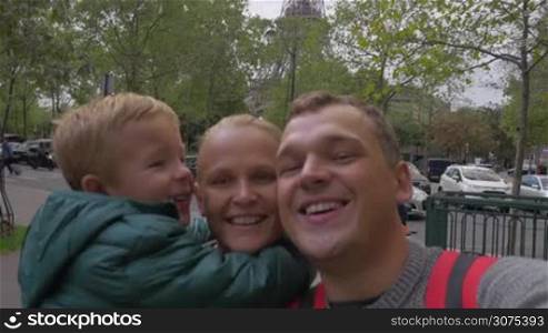 Happy family of mother, father and little son making selfie video against the Eiffel Tower. Visiting Paris, France