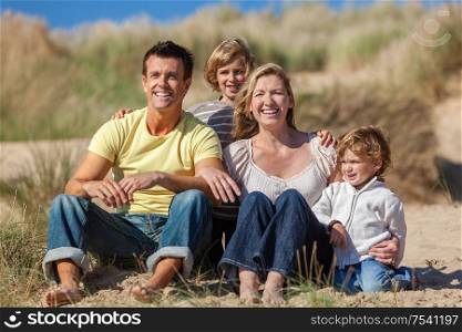 Happy family of mother, father and two sons, sitting laughing and having fun in the sand dunes of a sunny beach
