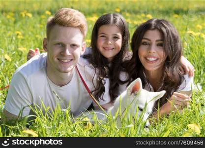Happy family of parents and daughter laying on grass in park with pet husky puppy dog. Family with dog in park