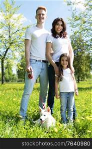 Happy family of parents and daughter with their dog in the park on a sunny day. Happy family with their dog