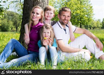 Happy family of parents and two children sitting on grass in spring park. Family in spring park