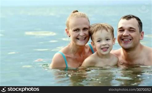 Happy family of young parents and son looking to the camera and smiling. Mother and father kissing child