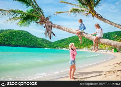 Happy family on a beach during summer vacation. Mom and kids on palmtree on caribbean beach