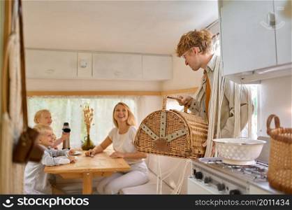 Happy family on the kitchen in trailer, summer camping. Couple with kids travel in camp car, motorhome interior on background. Campsite adventure, travelling lifestyle, vacation on rv vehicle. Happy family on kitchen in trailer, summer camping