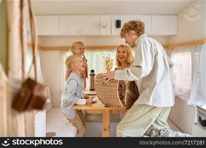 Happy family on the kitchen in trailer, summer camping. Couple with kids travel in camp car, motorhome interior on background. Campsite adventure, travelling lifestyle, vacation on rv-vehicle. Happy family on kitchen in trailer, summer camping