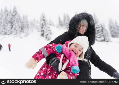 happy family on winter vacation, portrait of mother and cute little girl have fun and slide while snow falkes falling