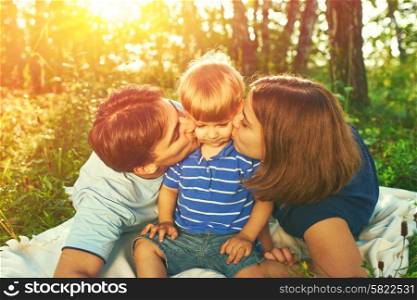Happy family outdoors. Parents kissing their child.