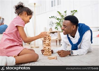 Happy family play game in living room. Mother, father and their little daughter poses at home together, good relationship. Mom, dad and female child, photo shoot in house. Happy family play game in living room