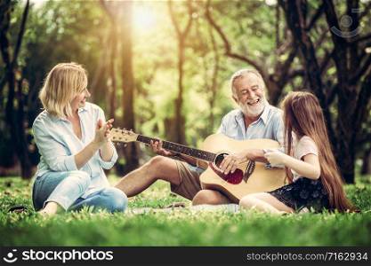 Happy family play guitar and sing together while sitting in the park in summer. Concept of family bonding by music.