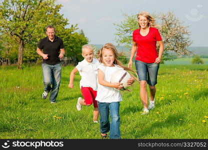 Happy family playing football, one child has grabbed the ball and is being chased by the others