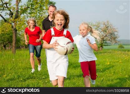 Happy family playing football, one child has grabbed the ball and is being chased by the others