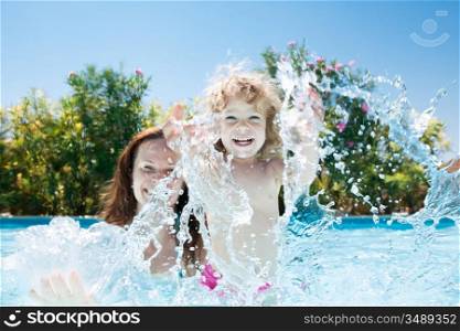 Happy family playing in blue water of swimming pool on a tropical resort at the sea. Summer vacations concept