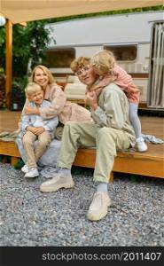Happy family poses at the trailer, summer camping. Parents with children travel in camp car, nature and forest on background. Campsite adventure, travelling lifestyle. Happy family poses at the trailer, summer camping