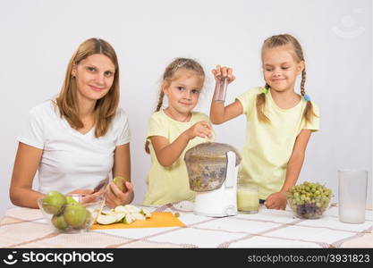 Happy family prepares freshly squeezed juice in a juicer. Young beautiful mother and two daughters sitting at a table squeezed juice from pears and grapes with a juicer