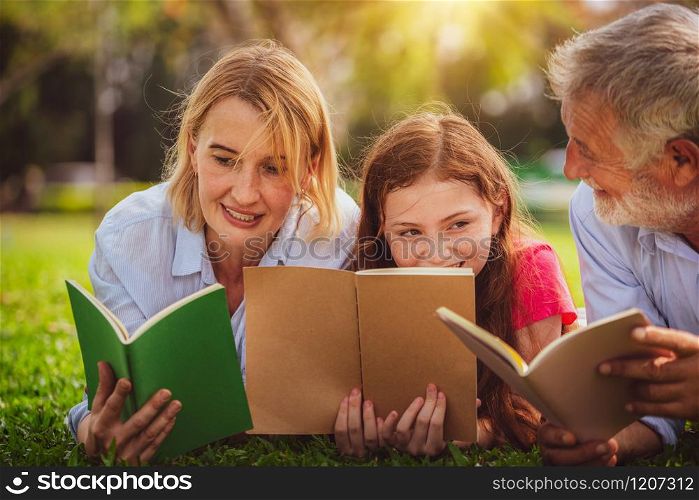 Happy family read books together and lying on green grass in public park. Little girl kid learning with mother and father in outdoors garden. Education and family lifestyle.. Happy family read books together in park garden.