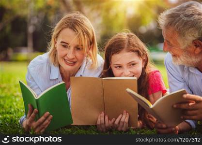 Happy family read books together and lying on green grass in public park. Little girl kid learning with mother and father in outdoors garden. Education and family lifestyle.. Happy family read books together in park garden.