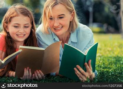 Happy family read books together and lying on green grass in public park. Little girl kid learning with mother in outdoors garden. Education and family lifestyle.. Happy family read books together in park garden.