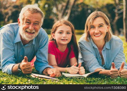 Happy family read books together and lying on green grass in public park. Little girl kid learning with mother and father in outdoors garden. Education and family lifestyle.. Happy family read books together in park garden.