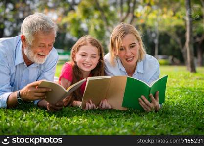 Happy family read books together and lying on green grass in public park. Little girl kid learning with mother and father in outdoors garden. Education and family lifestyle.