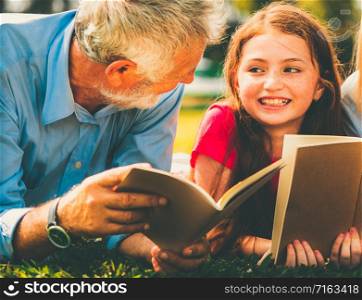 Happy family read books together and lying on green grass in public park. Little girl kid learning with father in outdoors garden. Education and family lifestyle.
