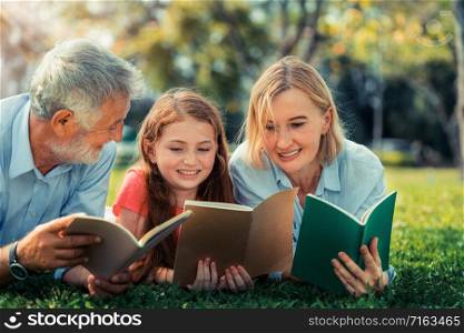 Happy family read books together and lying on green grass in public park. Little girl kid learning with mother and father in outdoors garden. Education and family lifestyle.