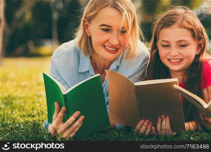 Happy family read books together and lying on green grass in public park. Little girl kid learning with mother in outdoors garden. Education and family lifestyle.