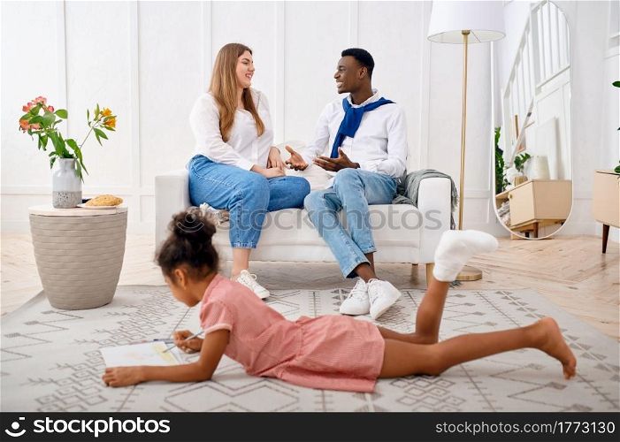 Happy family relaxing in living room. Mother, father and their little daughter poses at home together, good relationship. Mom, dad and female child, photo shoot in house. Happy family relaxing in living room