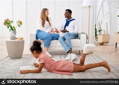 Happy family relaxing in living room. Mother, father and their little daughter poses at home together, good relationship. Mom, dad and female child, photo shoot in house. Happy family relaxing in living room