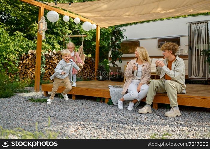Happy family resting at the motorhome, summer camping. Parents with children travel in camp car, nature and forest on background. Campsite adventure, travelling lifestyle. Happy family resting at motorhome, summer camping