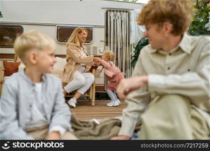 Happy family resting in the trailer, summer camping. Parents with children travel in camp car, nature and forest on background. Campsite adventure, travelling lifestyle. Happy family resting in trailer, summer camping