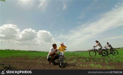 Happy Family Riding Bicycle. Father Helping Child Learn To Ride A Bike