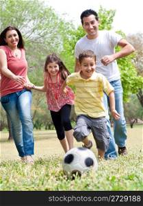 Happy family run to the soccer ball in the park, outdoor