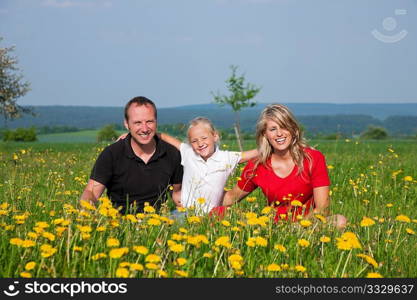 Happy family sitting in a meadow full of dandelions in spring (selective focus on girl)