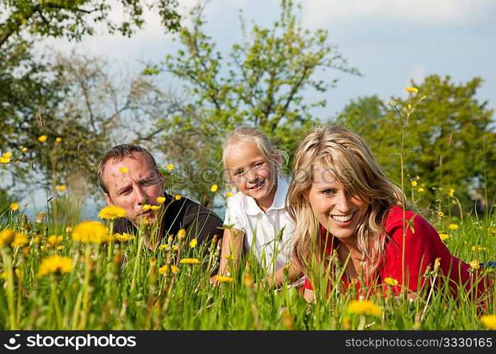 Happy family sitting in a meadow full of dandelions in spring (selective focus on girl)