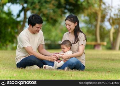 happy family sitting on a grass in the park. father and mother talking and playing with infant baby.