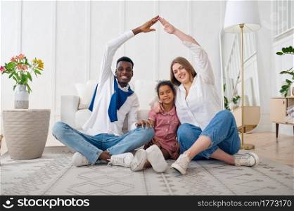 Happy family sitting on the floor in living room. Mother, father and their daughter poses at home together, good relationship. Happy family sitting on the floor in living room