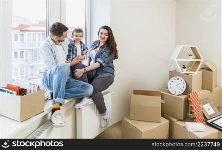 happy family sitting window sill with moving cardboard boxes their new home