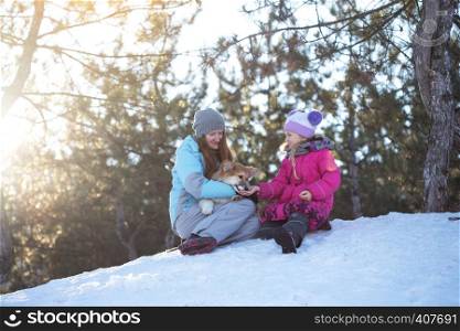 happy family - smiling mother and daughter with little cute corgi fluffy puppy at the winter day