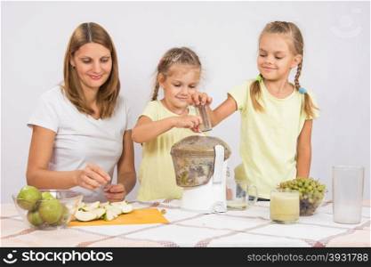 Happy family squeezes juice in a juicer. Young beautiful mother and two daughters sitting at a table squeezed juice from pears and grapes with a juicer