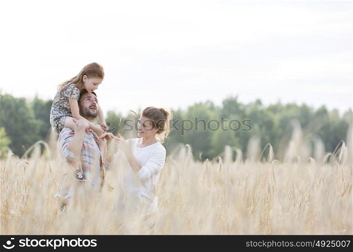 Happy family standing amidst wheat crops at farm against sky