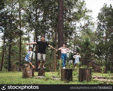 Happy family stands on wood natural seats in wild camp fire in the forest and smiling at the camera. Family spent time together on vacation. Ecotourism concept.