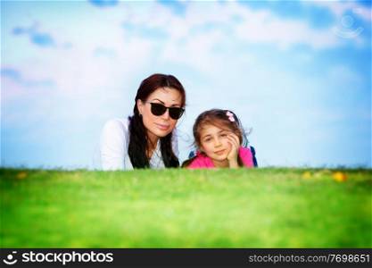 Happy family together, beautiful young mother with cute little daughter lying down on fresh green grass field in bright sunny day