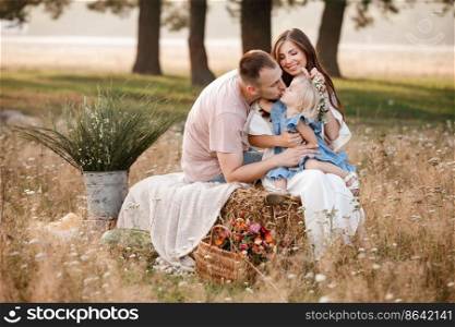 Happy family together  beautiful young parents in white clothes hugging their little daughter on straw stack in the park on a sunny summer day. happy holiday. mothers, fathers, babys day.. Happy family together  beautiful young parents in white clothes hugging their little daughter on straw stack in the park on a sunny summer day. happy holiday. mothers, fathers, babys day