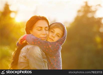 Happy family together, young beautiful mother closing eyes in pleasure hugging her cute little daughter, bright sunny day, happy motherhood