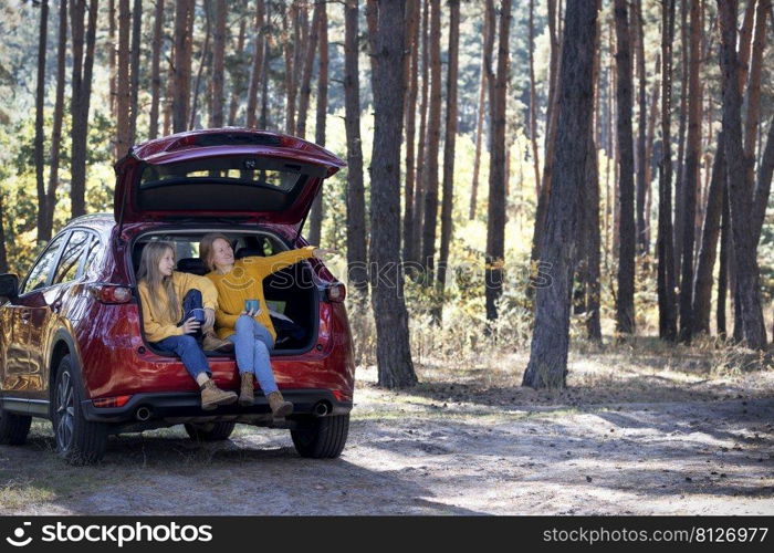 happy family travel by car. mother and daughter sitting in the trunk of a car 