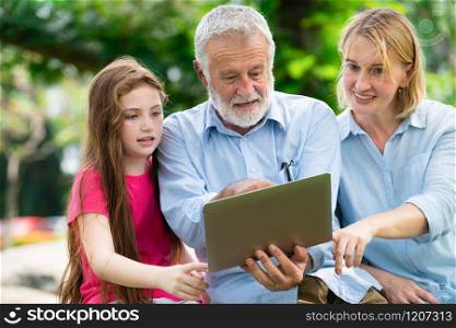 Happy family using laptop computer together in the garden park in summer. Kid education and family activities concept.. Happy family using laptop computer in public park.