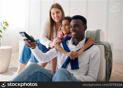 Happy family watching TV in living room. Mother, father and their daughter poses at home together, good relationship. Happy family watching TV in living room